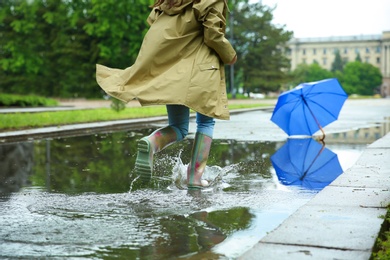 Photo of Woman in rubber boots running after umbrella on street, closeup. Rainy weather