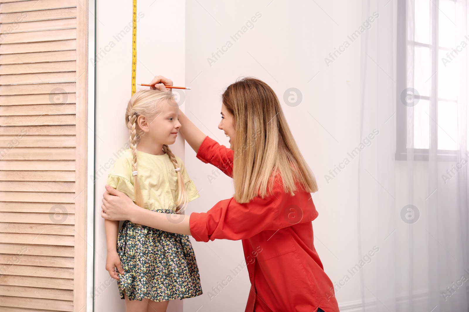 Photo of Young woman measuring her daughter's height at home