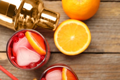 Tasty cranberry cocktail with ice cubes and orange in glasses on wooden table, flat lay