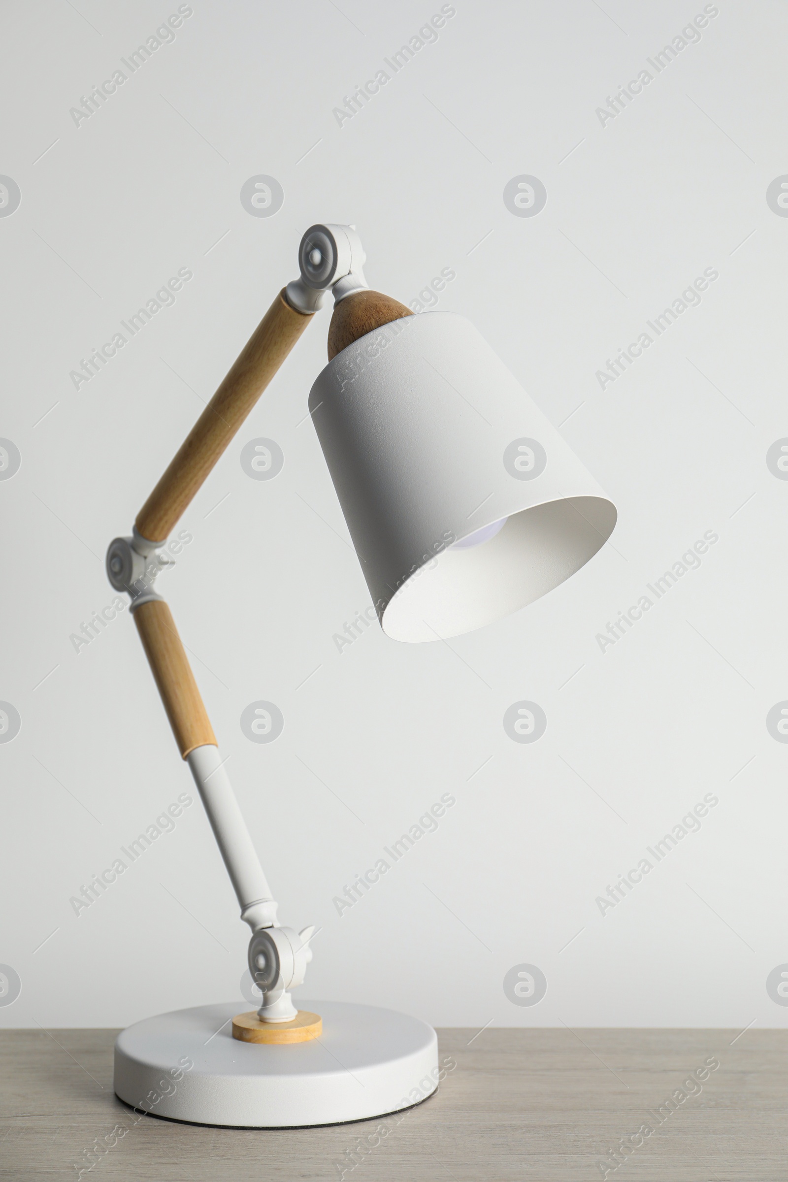 Stylish modern desk lamp on wooden table near white wall Photo of Stylish modern desk lamp on wooden table near white wall