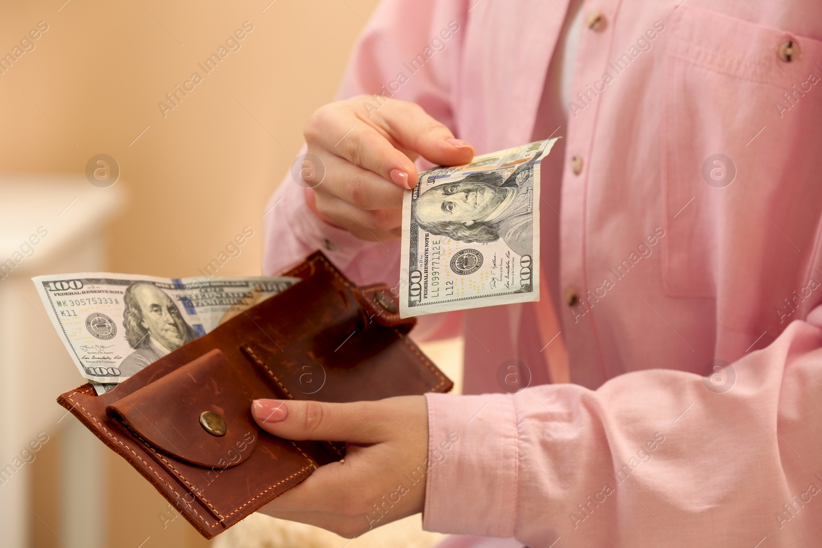 Photo of Woman giving 100 dollar bill and holding brown leather wallet with banknotes indoors, closeup. Money exchange