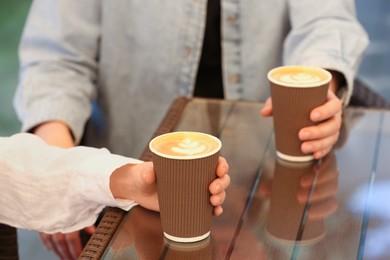 Women holding takeaway paper cups at table, closeup. Coffee to go