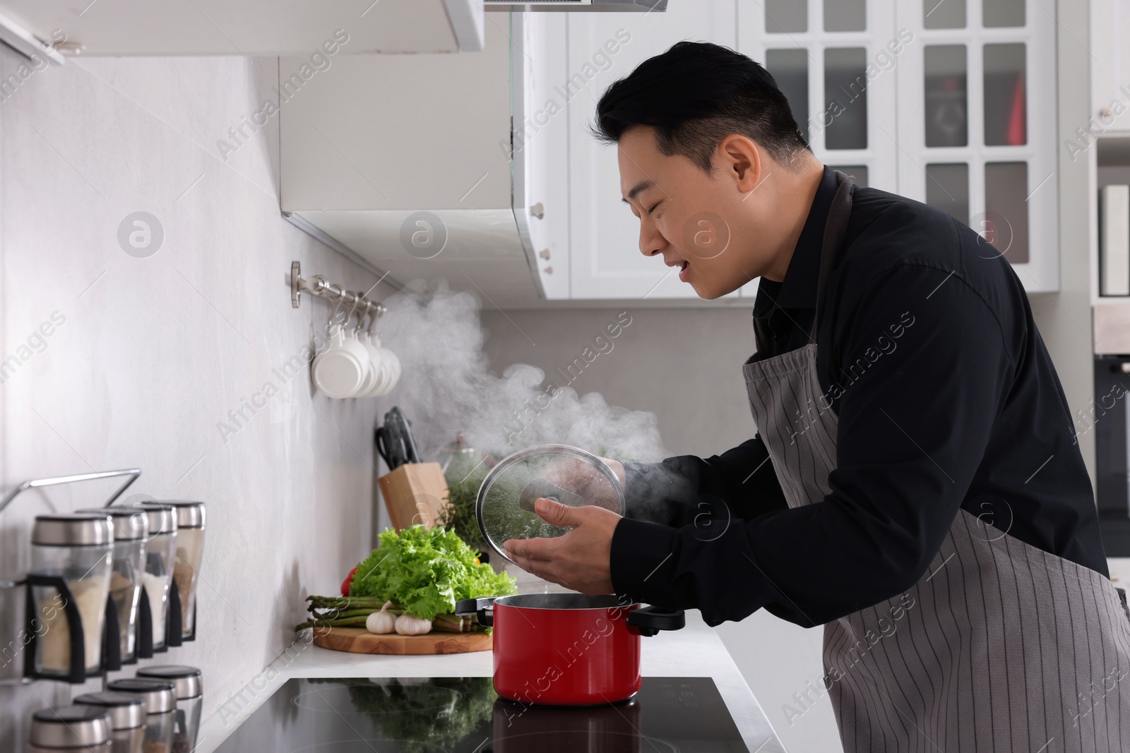 Photo of Man cooking and smelling dish on cooktop in kitchen