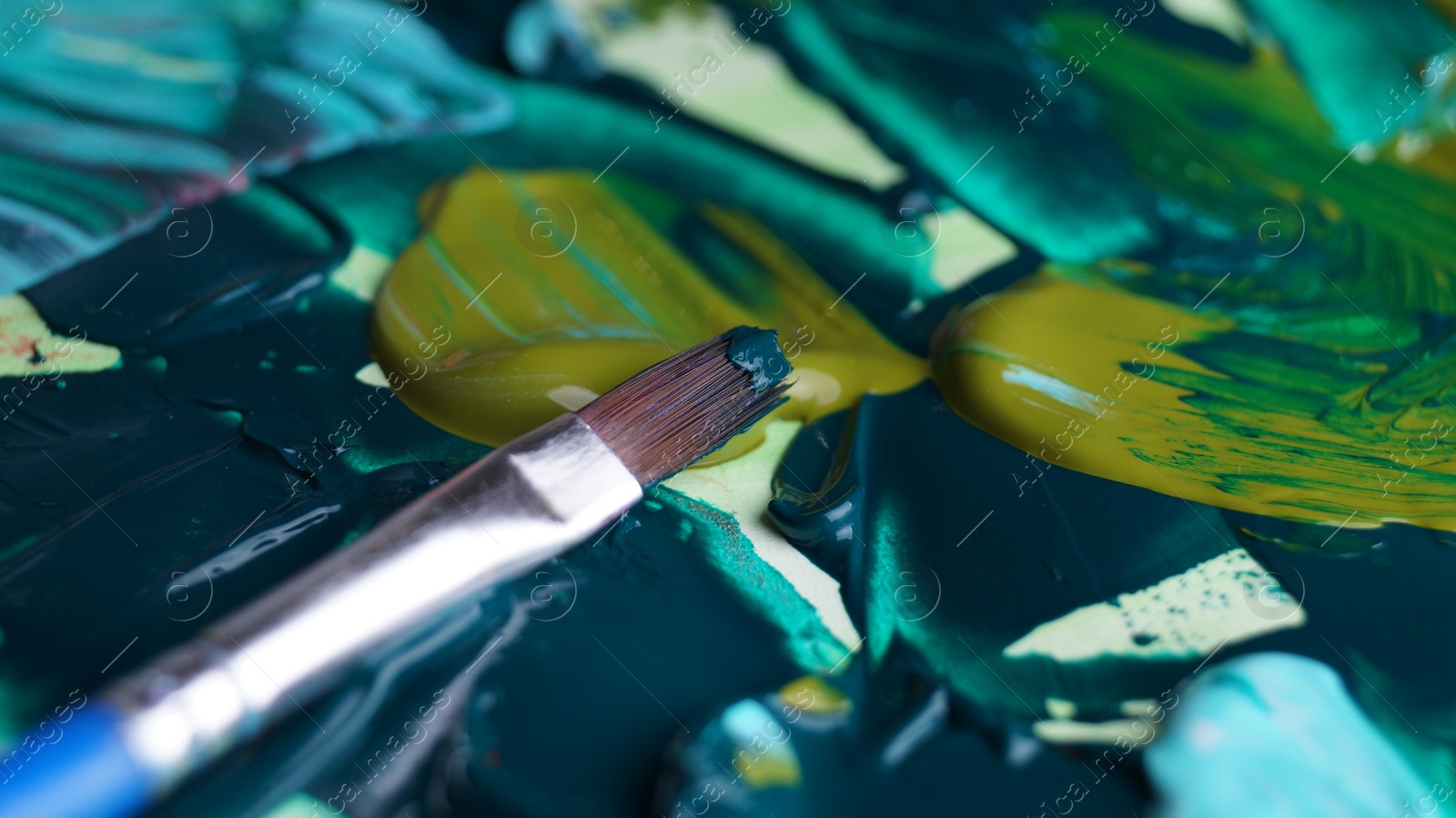 Photo of Brush on artist's palette with mixed paints, closeup