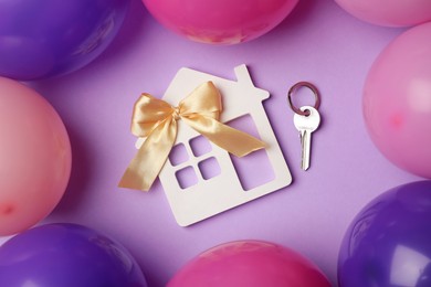 Photo of House model with bow, key and colorful balloons on violet background, flat lay. Housewarming party