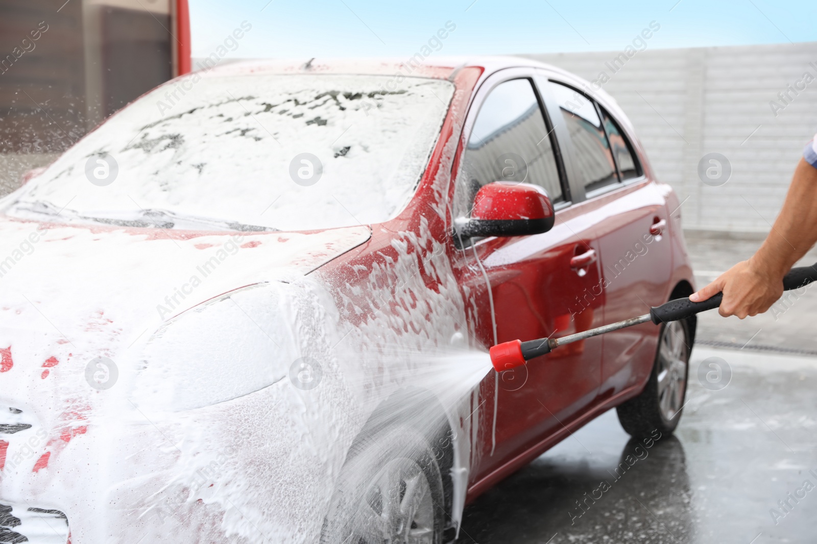 Photo of Man foaming red auto at car wash. Cleaning service