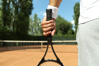 Sportsman with racket at tennis court, closeup