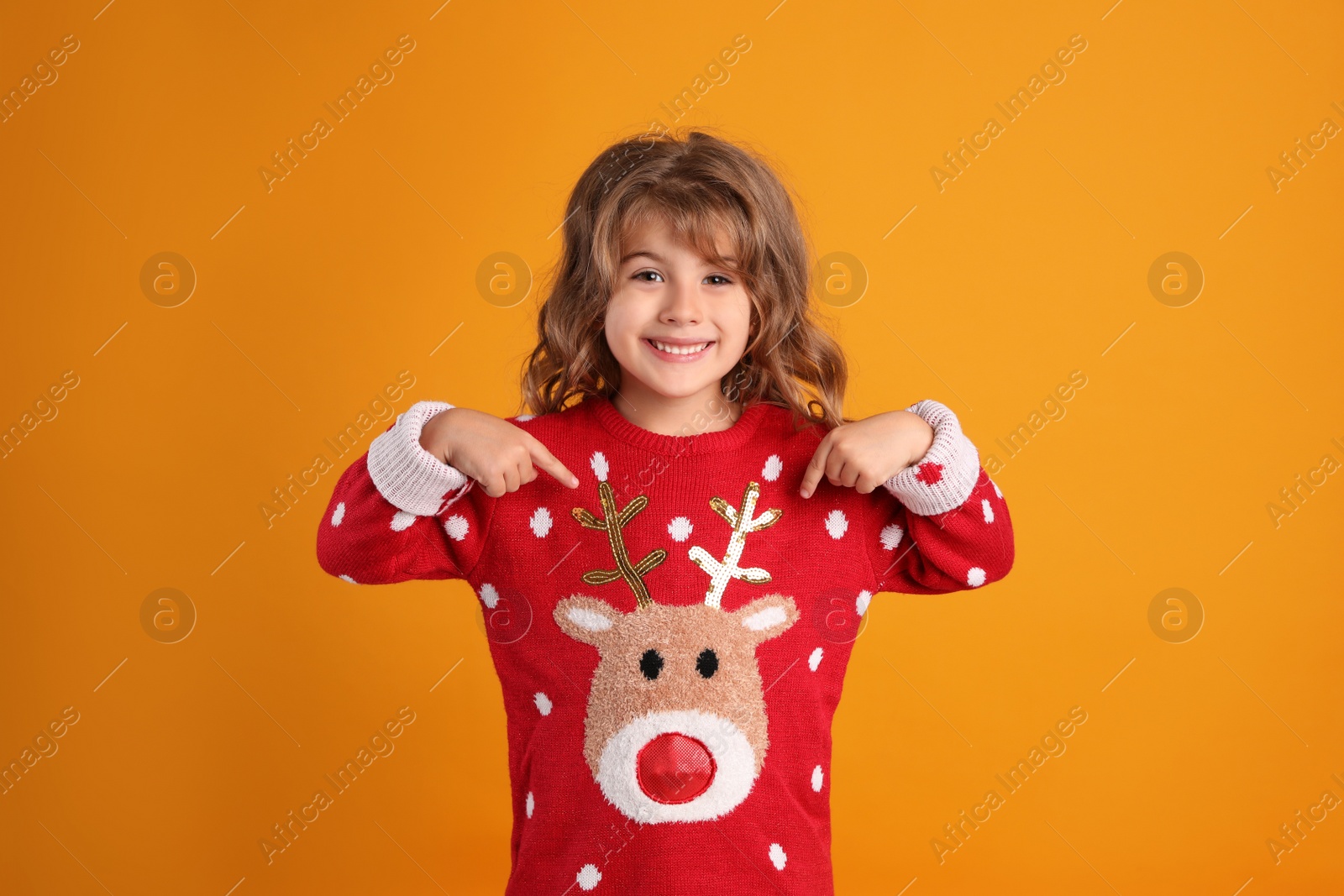 Photo of Cute little girl pointing at her red Christmas sweater against orange background