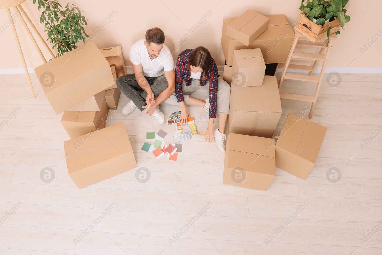 Photo of Happy couple surrounded by moving boxes choosing colors in new apartment, above view