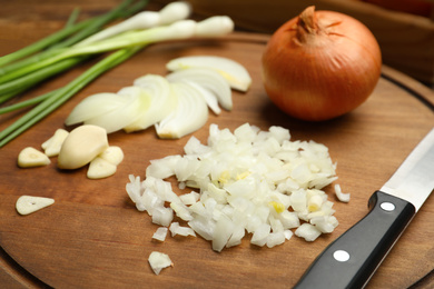 Photo of Board with cut onion and garlic on wooden table, closeup