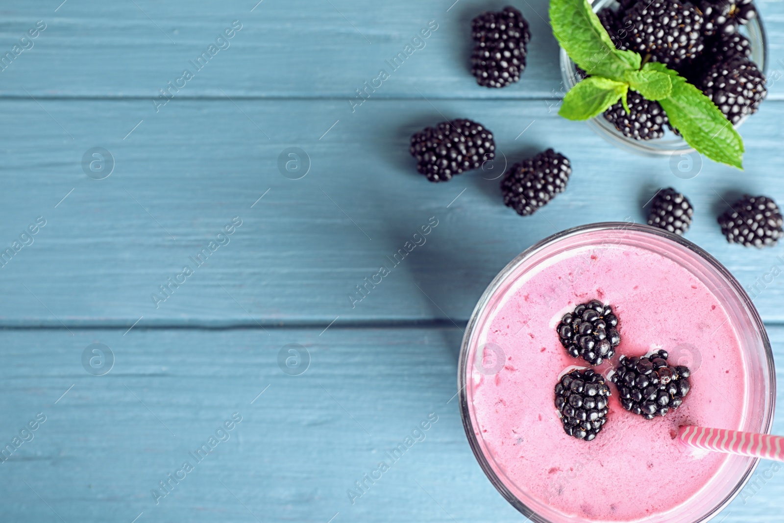 Photo of Flat lay composition with glass of delicious blackberry smoothie on blue wooden background. Space for text