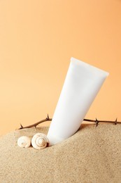 Photo of Tube with cream, shells and branches on sand against orange background. Cosmetic product