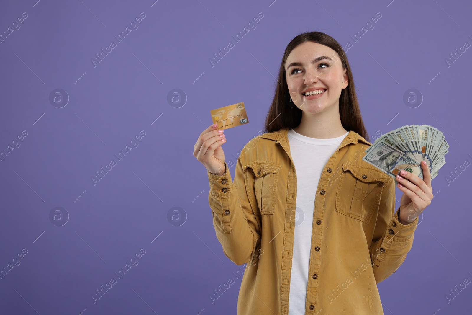 Photo of Happy woman with credit card and dollar banknotes on purple background, space for text