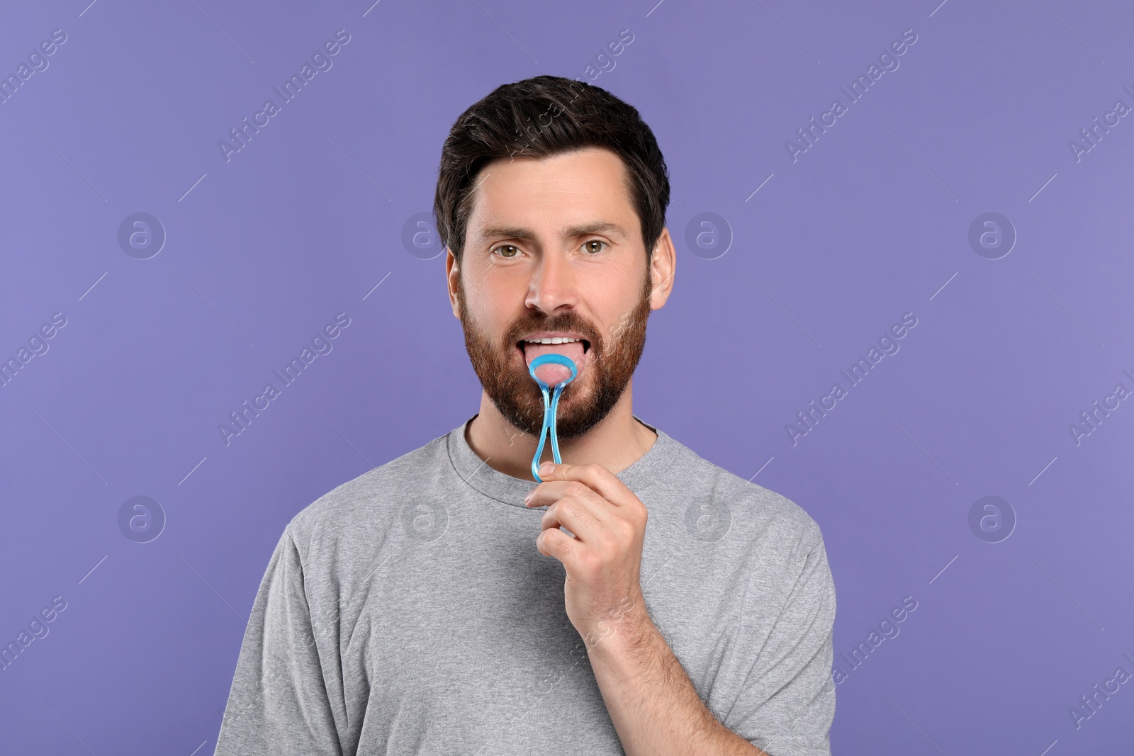 Photo of Handsome man brushing his tongue with cleaner on violet background