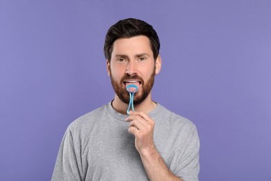Photo of Handsome man brushing his tongue with cleaner on violet background