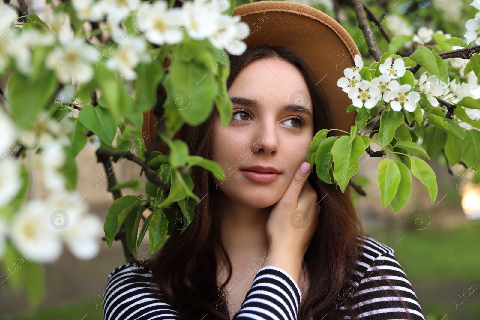 Photo of Beautiful woman in hat near blossoming tree on spring day