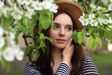 Photo of Beautiful woman in hat near blossoming tree on spring day