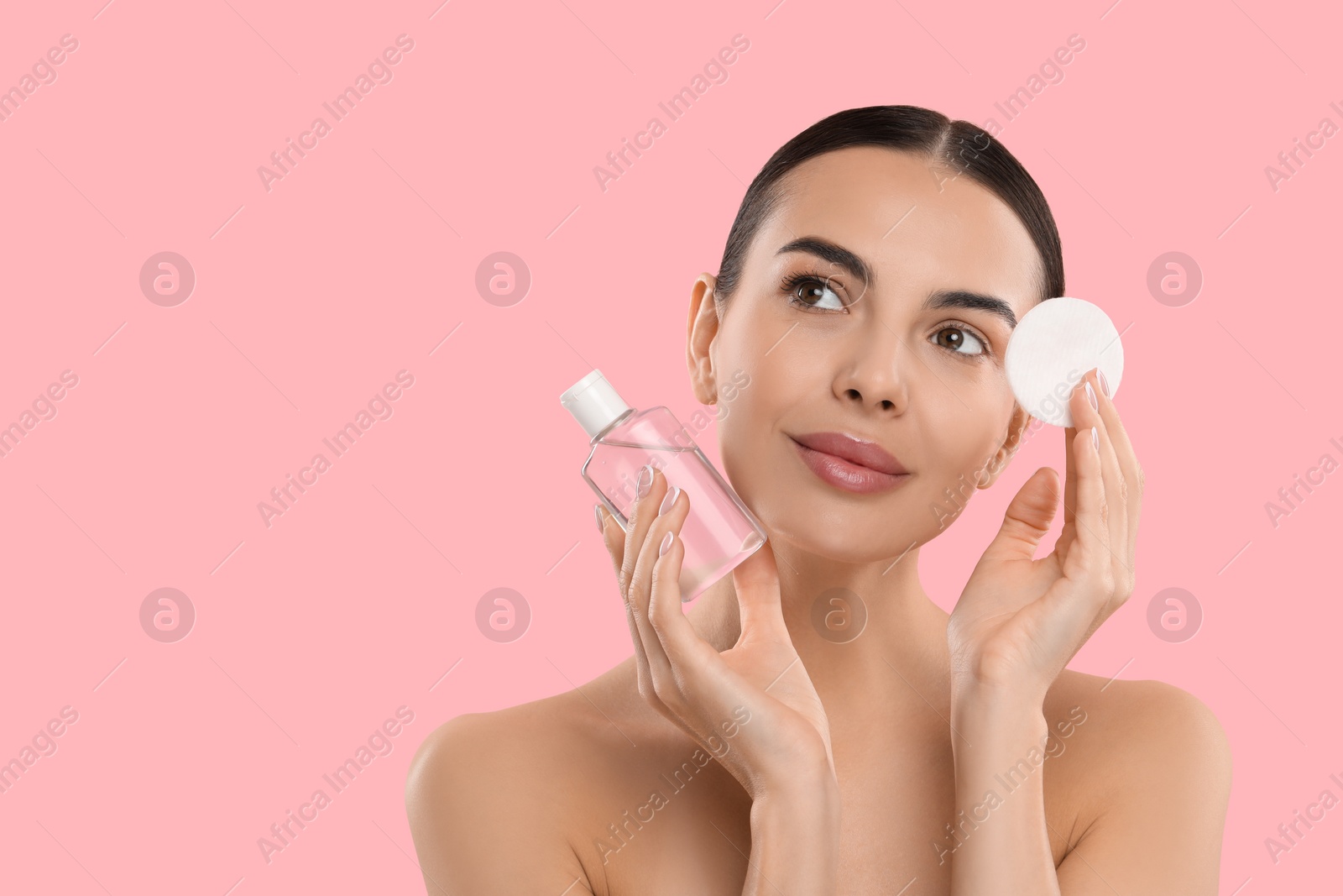 Photo of Beautiful woman holding makeup remover and cotton pad on pink background, space for text