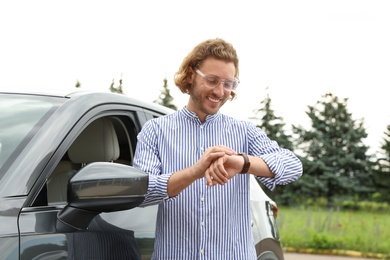 Photo of Attractive young man checking time near luxury car outdoors