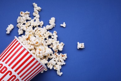 Photo of Bucket of tasty popcorn on blue background, flat lay. Space for text