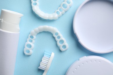 Photo of Bite correction. Toothpaste, brush, container and dental mouth guards on light blue background, flat lay