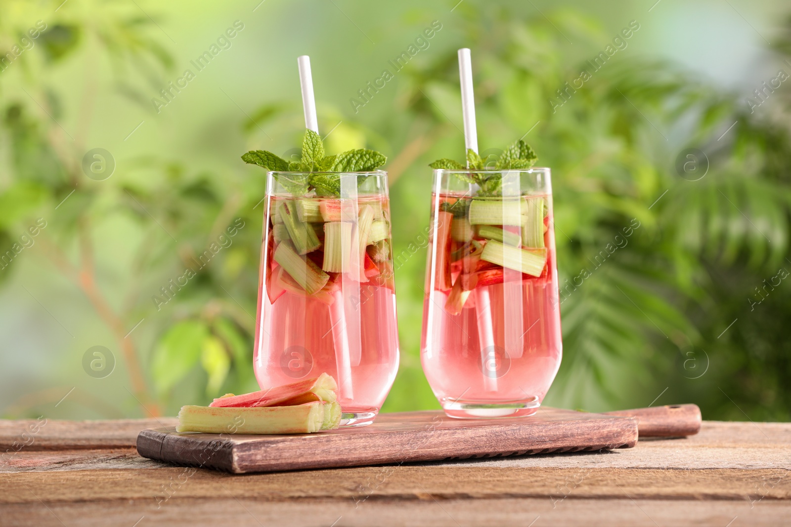 Photo of Glasses of tasty rhubarb cocktail on wooden table outdoors