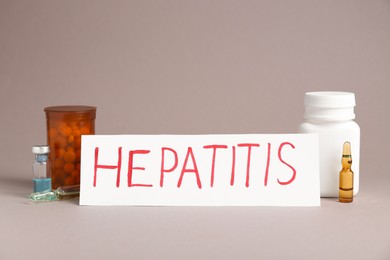 Photo of Word Hepatitis, vials and bottles of pills on beige background