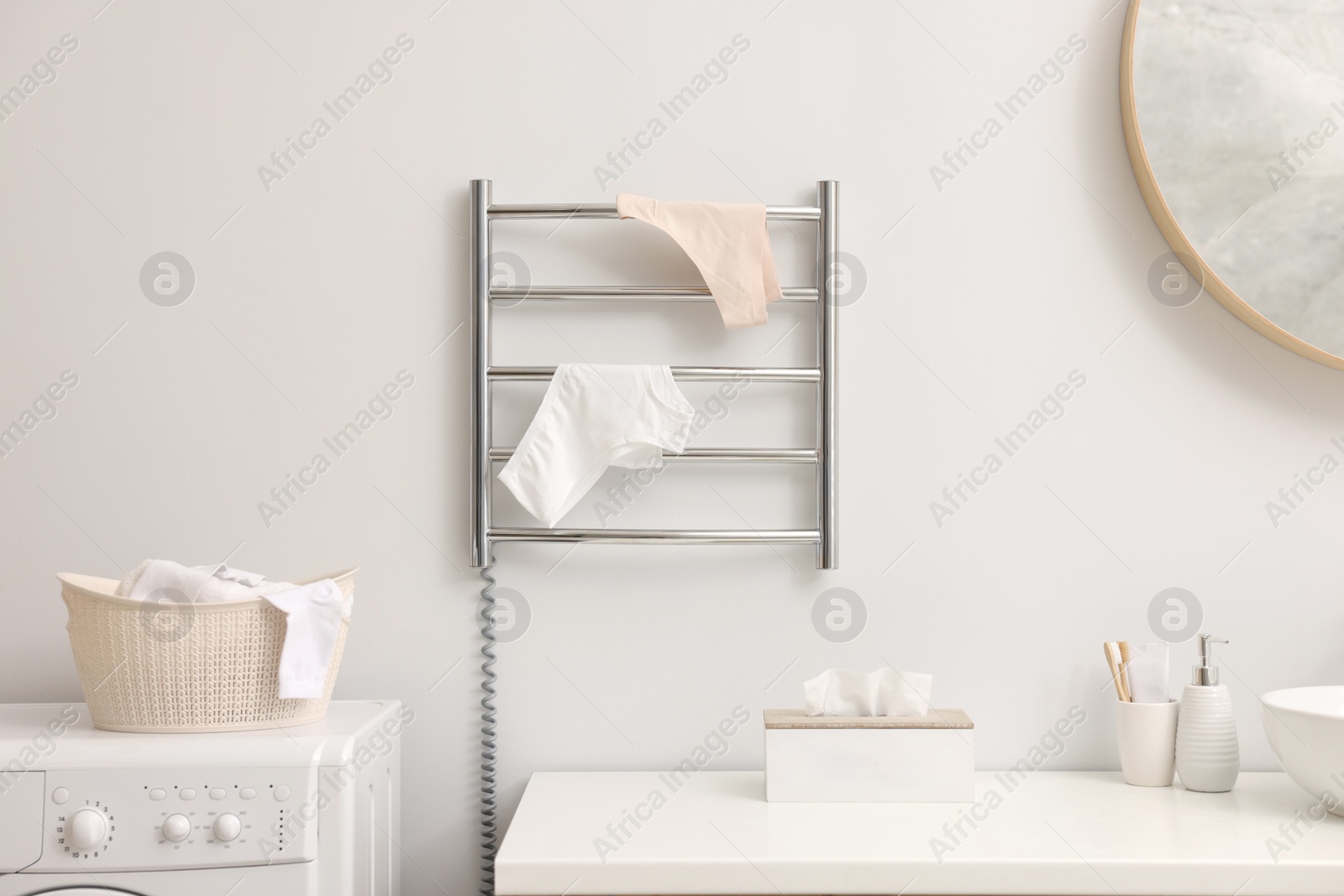 Photo of Heated towel rail with underwear on white wall in bathroom