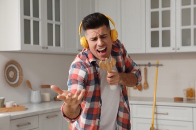 Photo of Man with headphones and fork spatula singing in kitchen