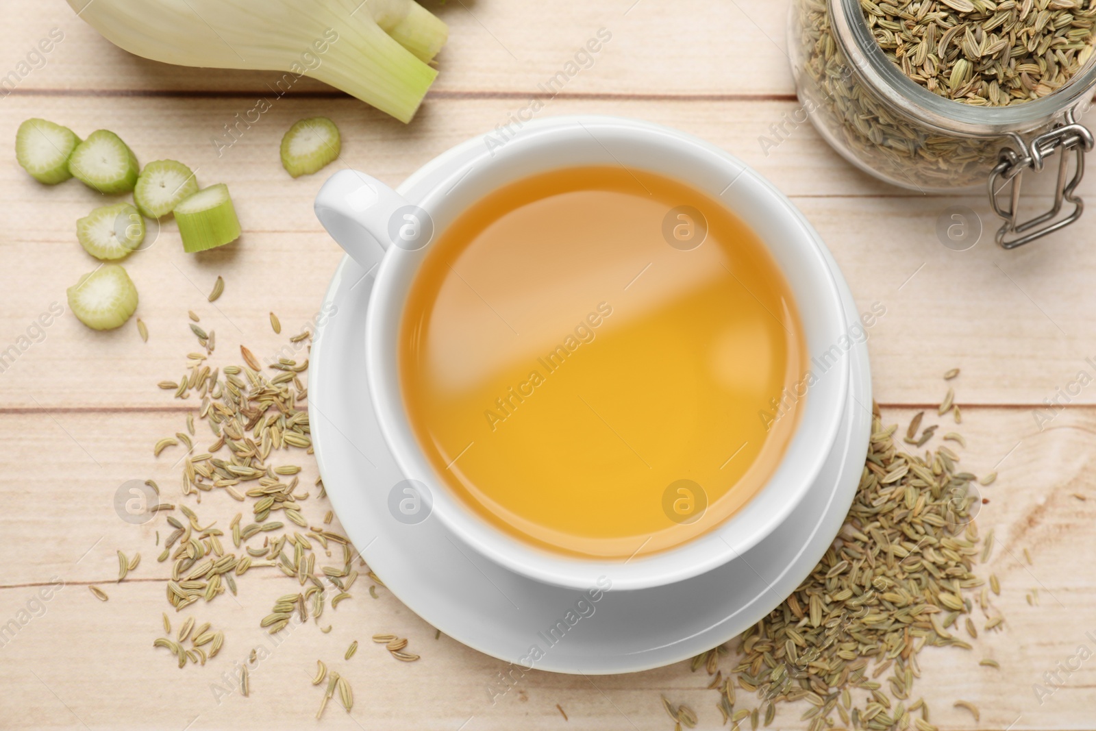 Photo of Fennel tea in cup, seeds and fresh vegetable on light wooden table, flat lay