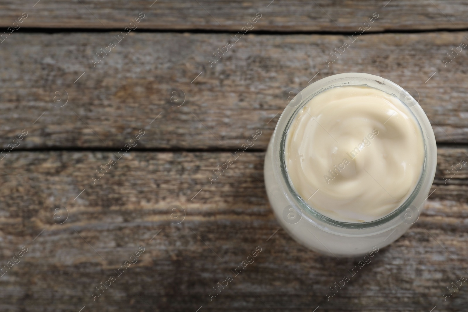 Photo of Fresh mayonnaise sauce in glass jar on wooden table, top view. Space for text