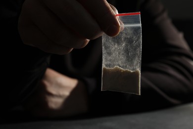 Photo of Drug addiction. Man with plastic bag of cocaine at grey table, selective focus