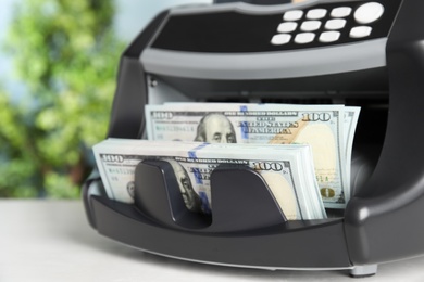 Modern electronic bill counter with money on table indoors, closeup