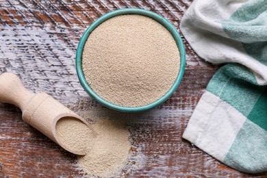 Photo of Bowl and scoop with active dry yeast on wooden table, flat lay