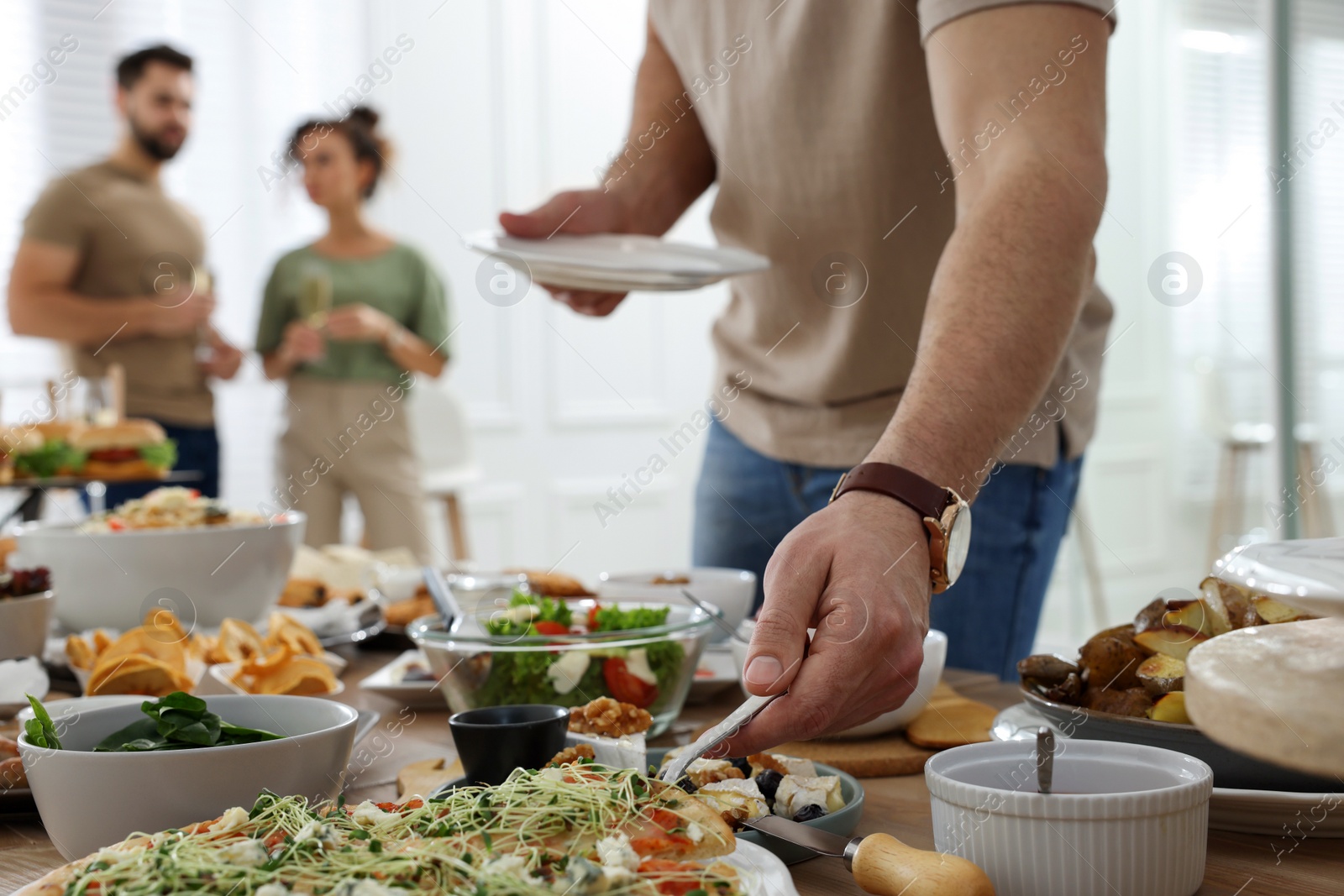 Photo of Man taking slice of pizza from buffet indoors, closeup. Brunch table setting