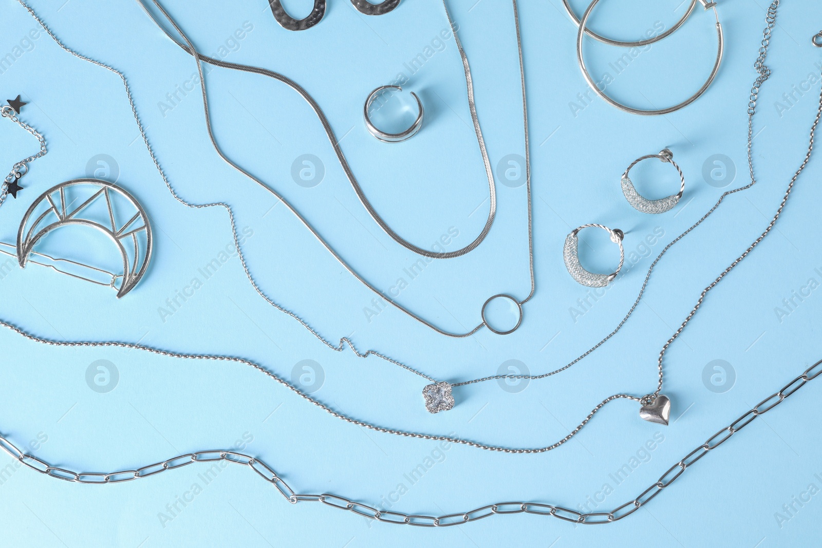 Photo of Metal chains and other different accessories on light blue background, flat lay. Luxury jewelry