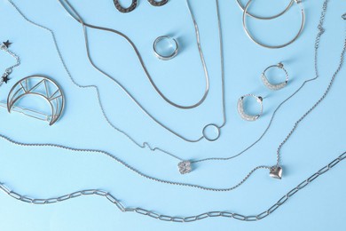 Metal chains and other different accessories on light blue background, flat lay. Luxury jewelry