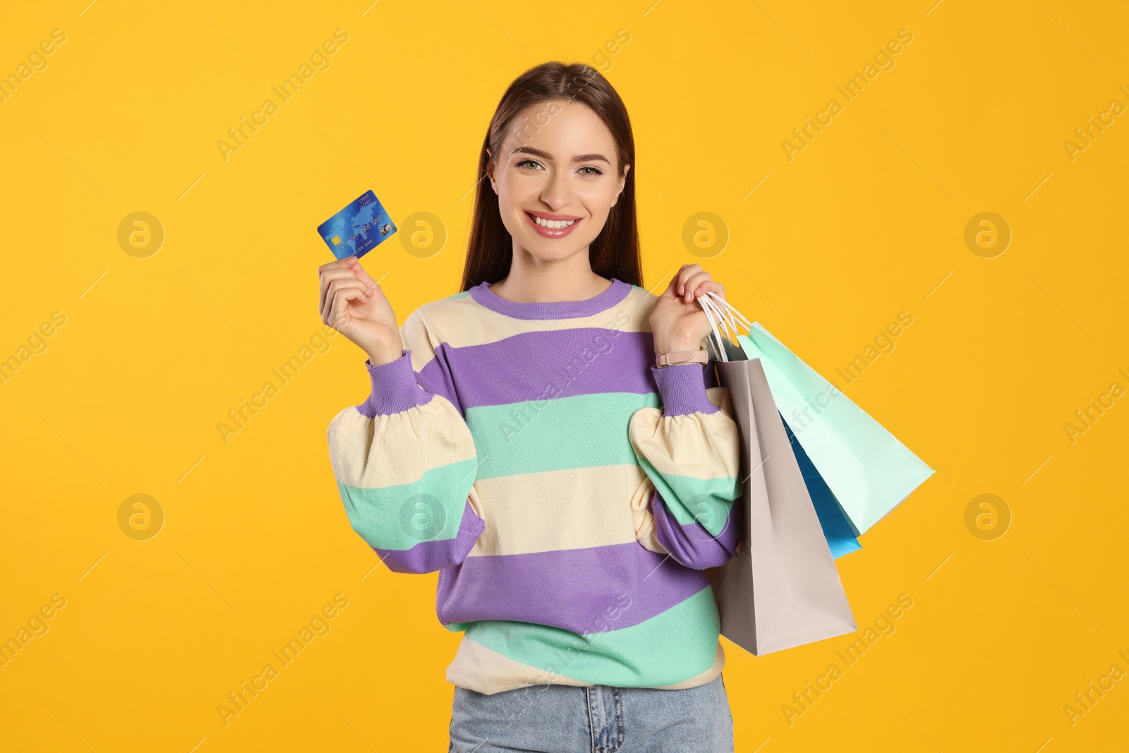 Photo of Happy young woman with shopping bags and credit card on yellow background. Big sale