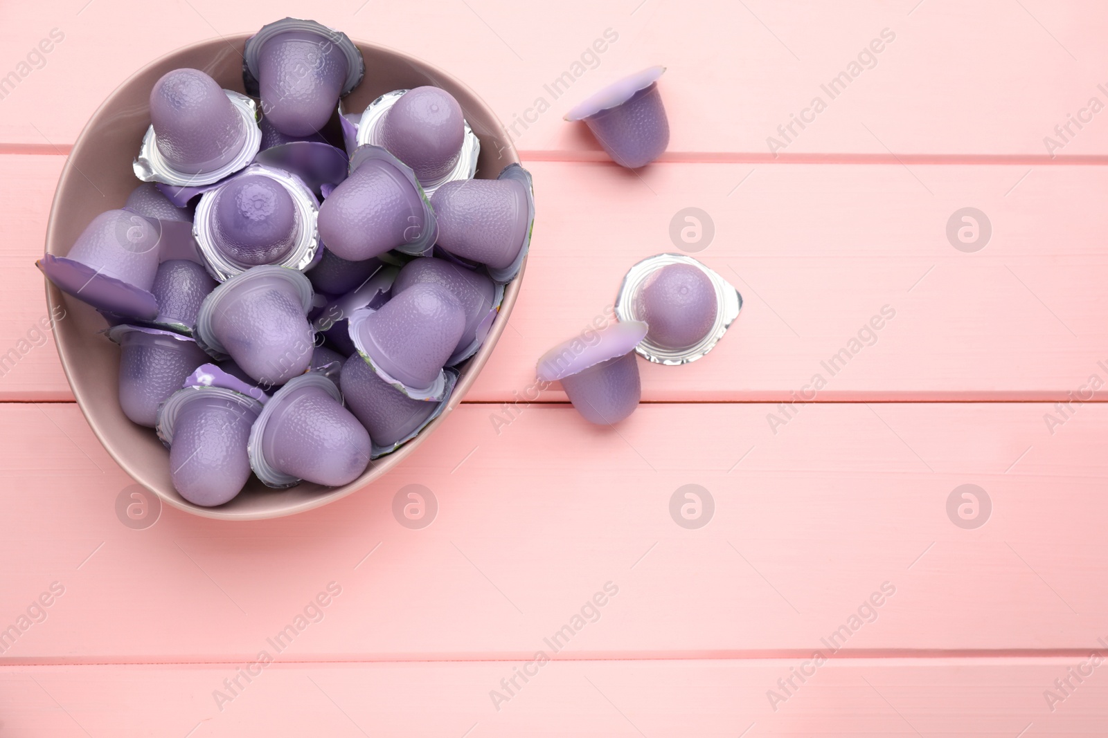 Photo of Bowl with tasty bright jelly cups on pink wooden table, flat lay. Space for text