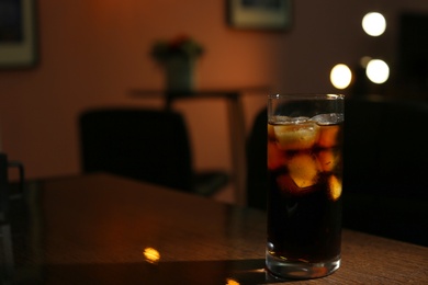 Photo of Glass of cold cola on table in dark room. Space for text