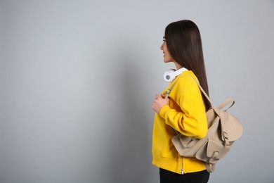 Photo of Beautiful young woman with stylish leather backpack and headphones on grey background. Space for text