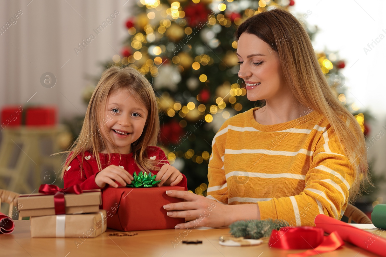 Photo of Christmas presents wrapping. Mother and her little daughter decorating gift box with bow at home