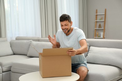 Happy man opening parcel on sofa at home. Internet shopping