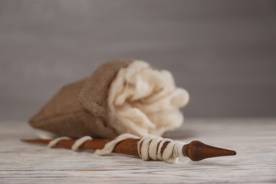 Soft white wool and spindle on wooden table. Space for text