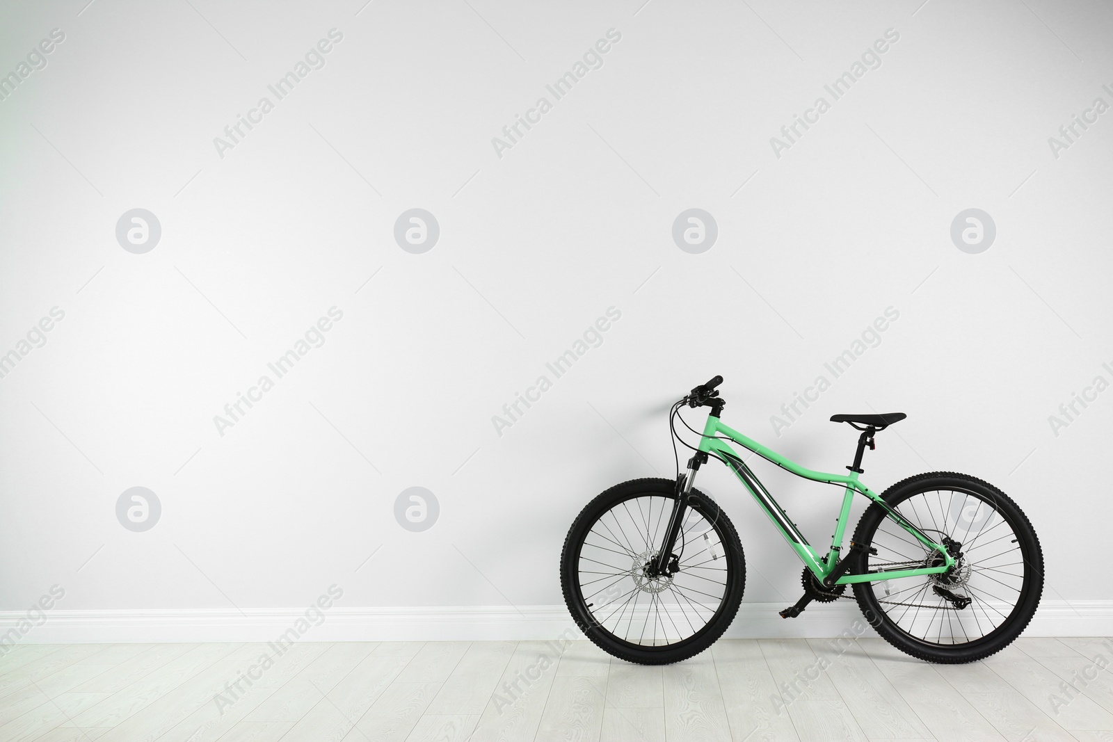 Photo of Modern bicycle near white wall indoors. Space for text