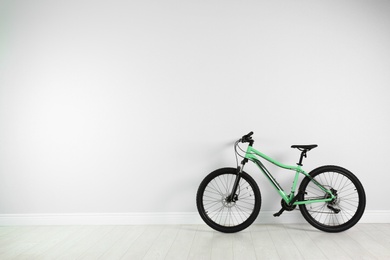 Modern bicycle near white wall indoors. Space for text