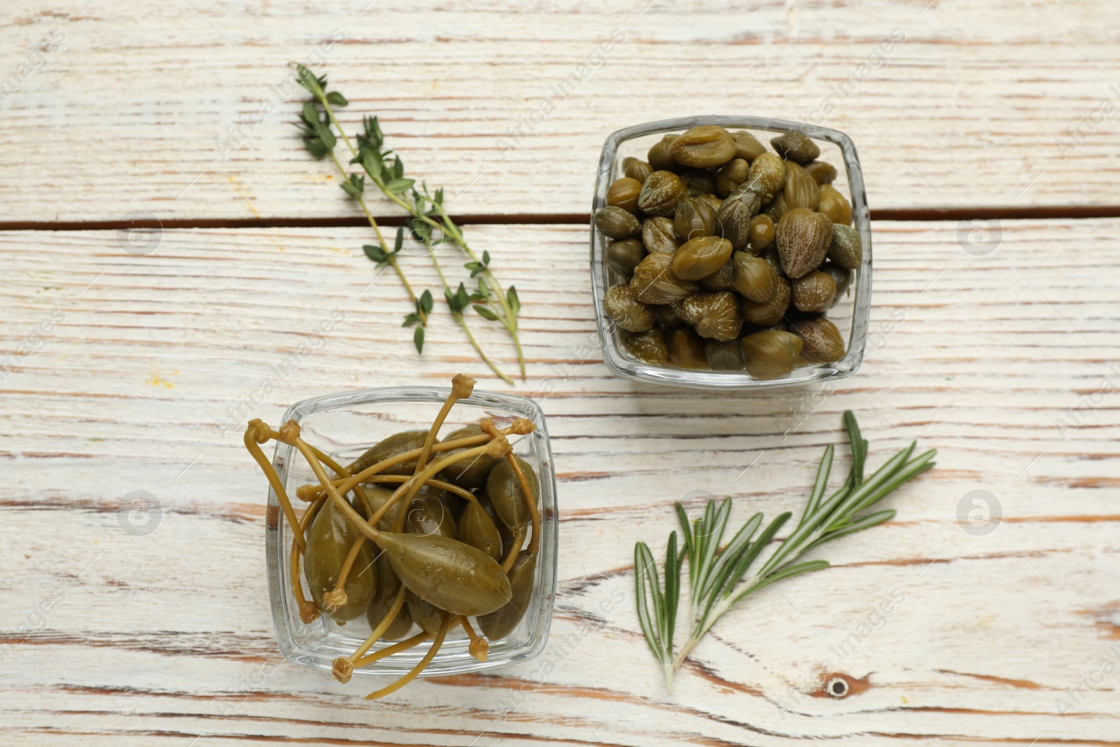 Photo of Tasty capers, rosemary and thyme on white wooden table, flat lay