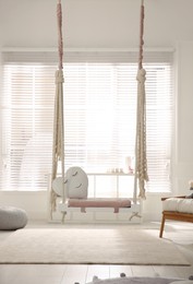 Photo of Beautiful swing with toy heart in room. Stylish interior design
