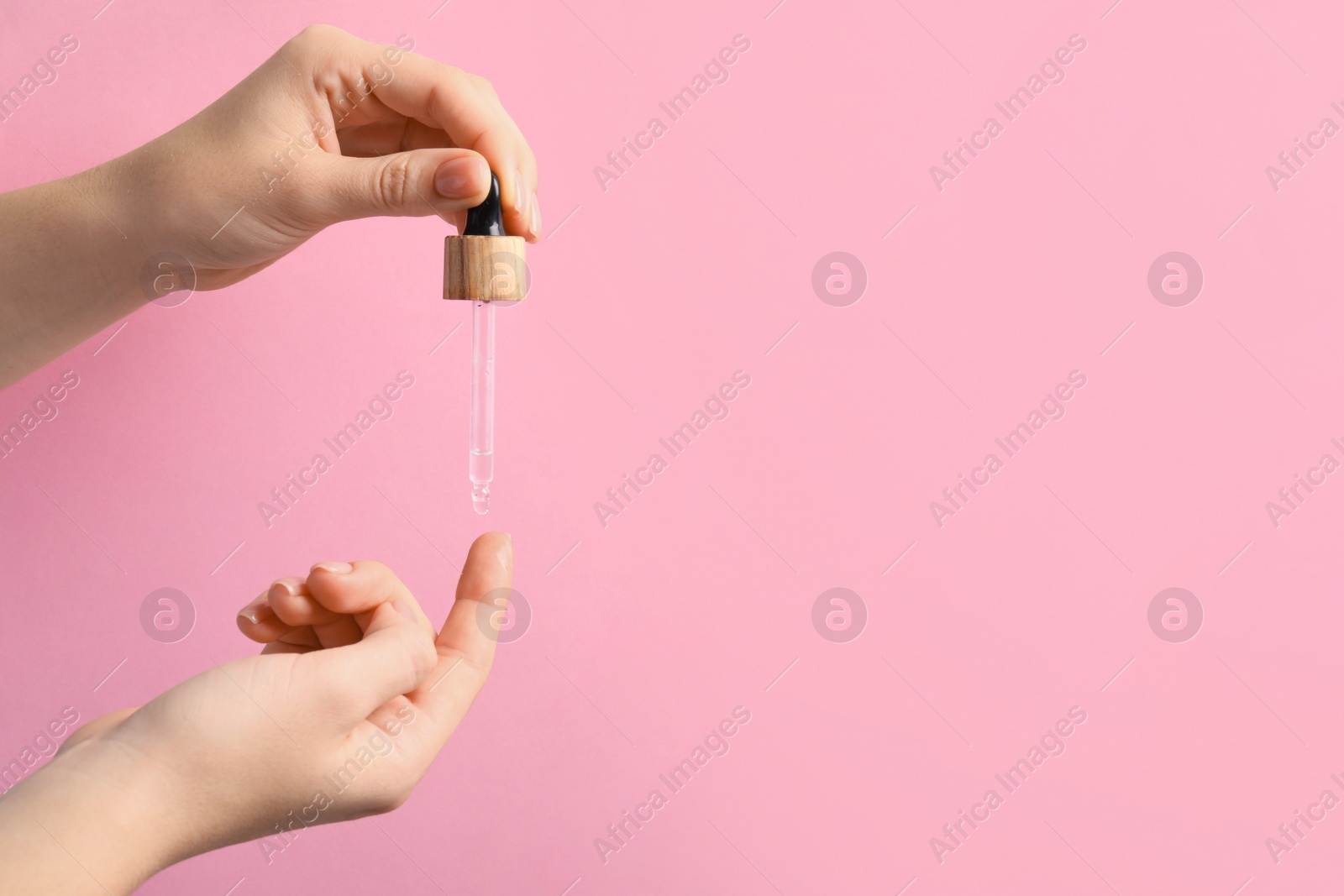 Photo of Woman dripping serum from pipette on her finger against pink background, closeup. Space for text