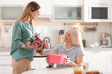 Daughter congratulating happy mature woman on Mother's Day at home